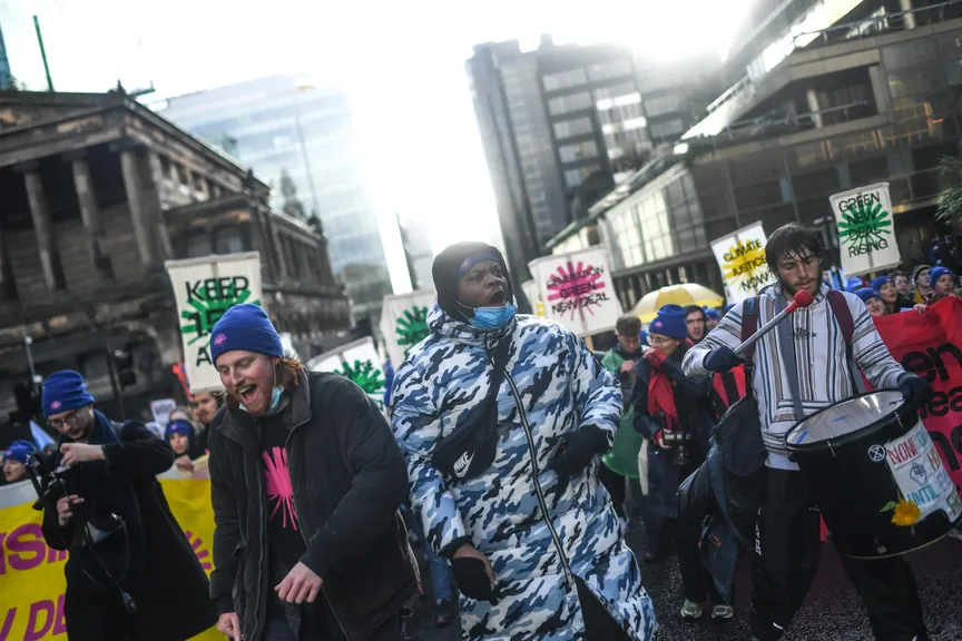 A group of young people march through a central city street, holding Green New Deal Rising banners.